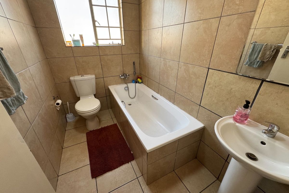 A functional bathroom featuring a bathtub, pedestal basin, and toilet with neutral wall and floor tiling.