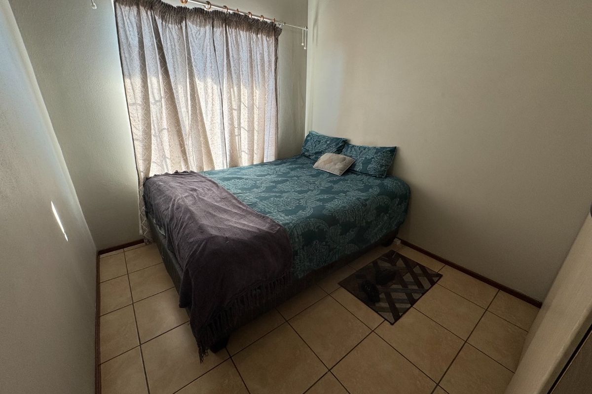 A compact bedroom featuring neutral wall finishes and tiled flooring, providing a functional space with natural light from the window.