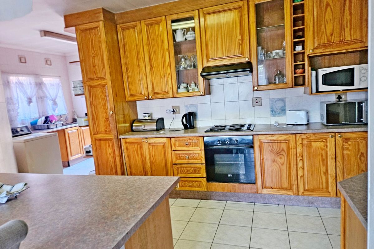 A functional kitchen featuring traditional wooden cabinetry, built-in oven, hob, extractor fan, and tiled flooring, with an adjacent laundry area visible.