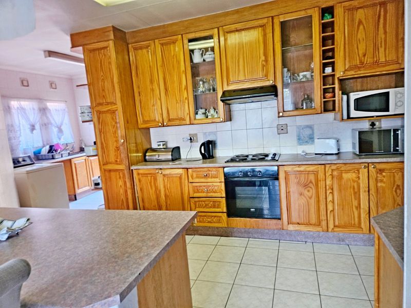 A functional kitchen featuring traditional wooden cabinetry, built-in oven, hob, extractor fan, and tiled flooring, with an adjacent laundry area visible.