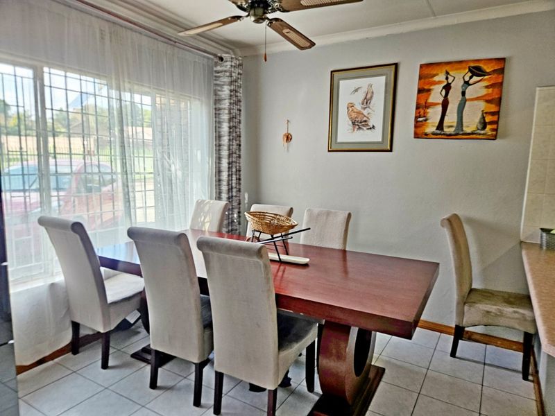 A dining room featuring tiled flooring, a ceiling fan, and large windows with security bars, providing a functional space for meals.