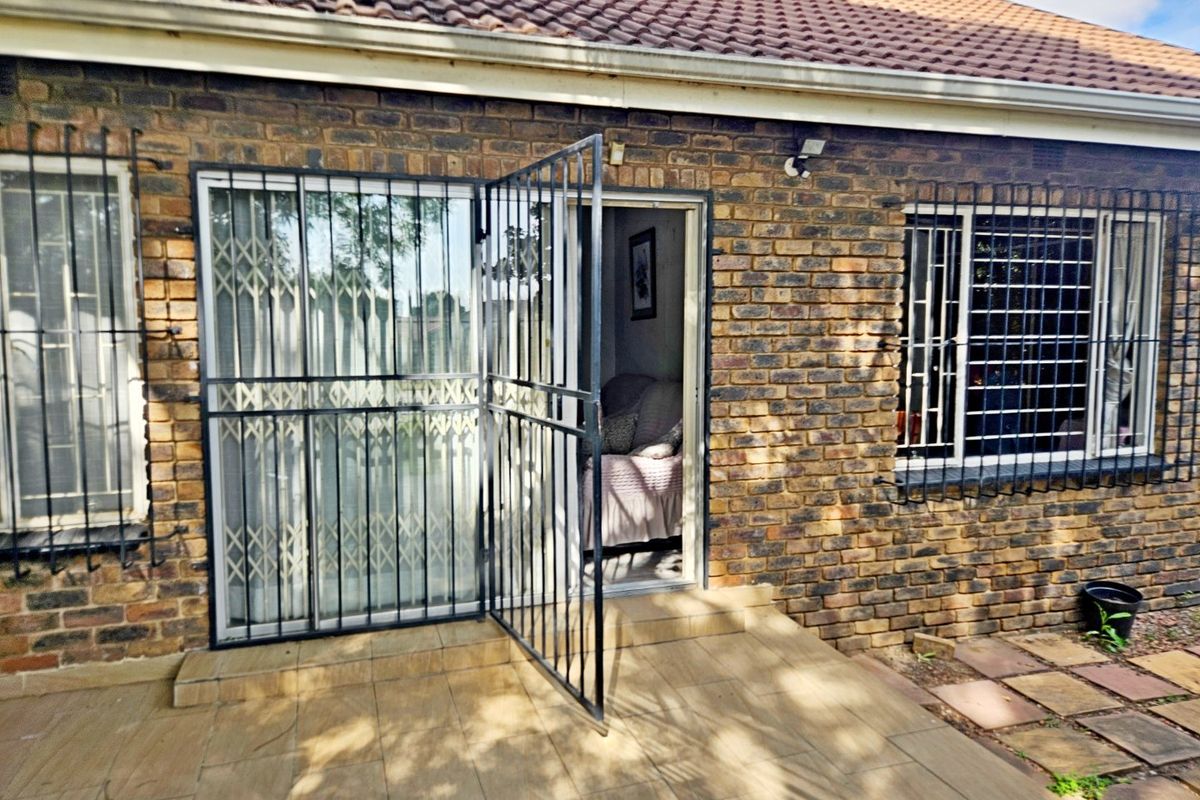 Rear exterior view of the townhouse featuring a face brick facade, tiled patio area, and secure metal security gates and window bars.