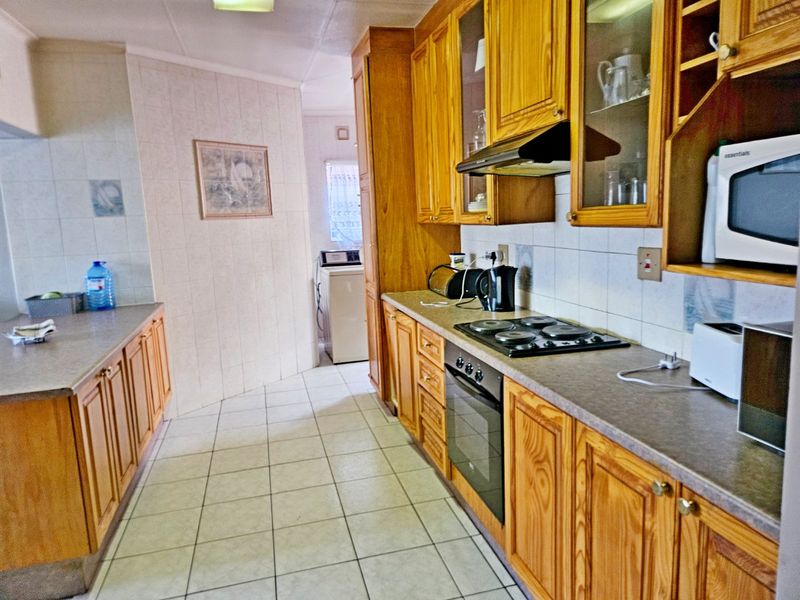 A functional kitchen featuring traditional wooden cabinetry, built-in oven, hob, extractor fan, and tiled flooring, offering a classic layout with ample storage space.