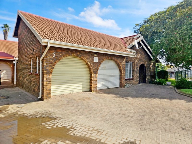 Front exterior view of a townhouse featuring a double garage with arched brick detailing, a tiled roof, and a paved driveway.