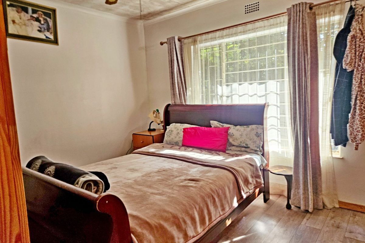 A bedroom featuring laminate flooring, a ceiling fan, and a window fitted with security bars.