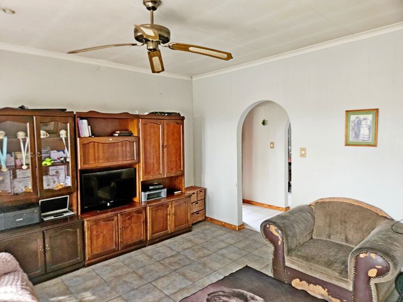 A living room featuring tiled flooring, a ceiling fan, and an arched doorway leading to an adjacent space.