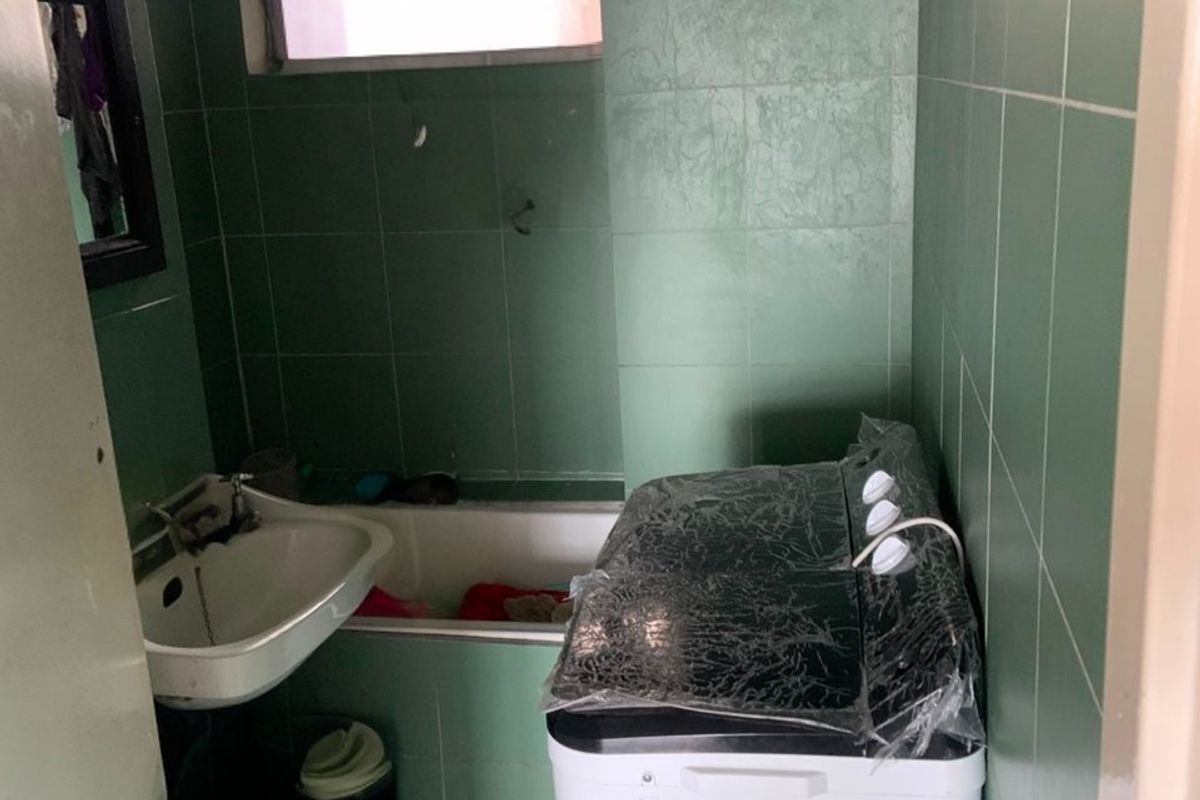 A compact bathroom featuring green wall tiles, a built-in bathtub, and a wall-mounted basin, requiring modernization to improve functionality and aesthetic appeal.