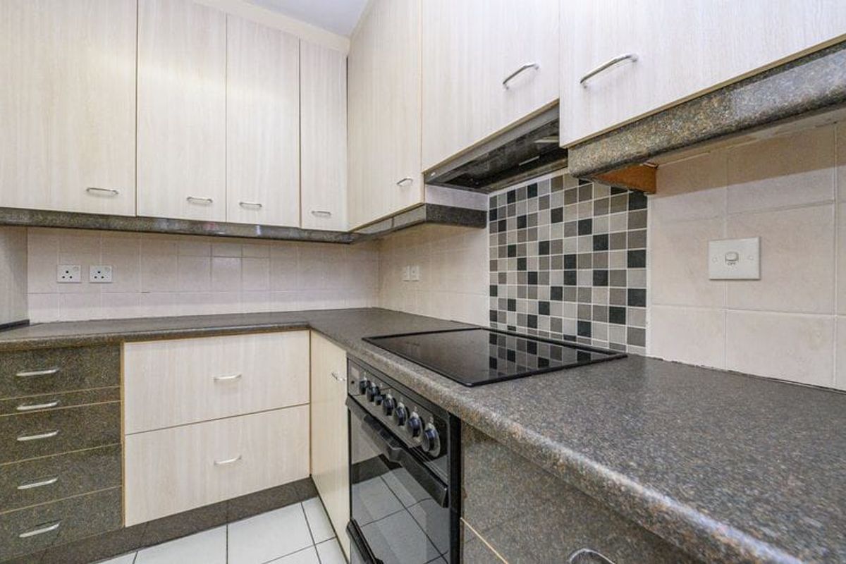 A functional kitchen featuring light wood-tone cabinetry, dark stone countertops, a built-in electric oven and hob, and a decorative mosaic tile backsplash.