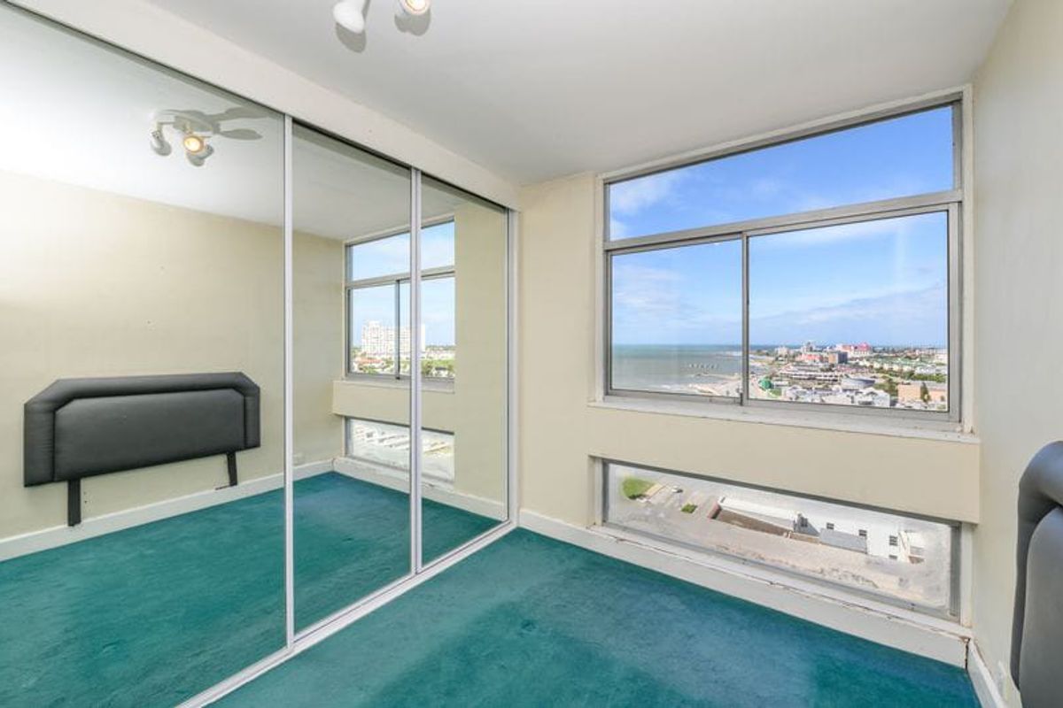 A bedroom featuring large sliding windows with coastal views, mirrored built-in wardrobes, and carpet flooring, offering a bright space with potential for modernization.