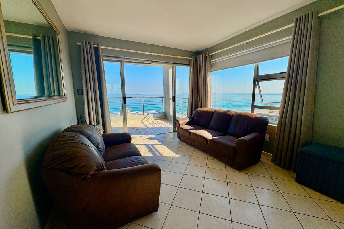Bright living room featuring tiled floors and large sliding glass doors that open onto a balcony with expansive ocean views.