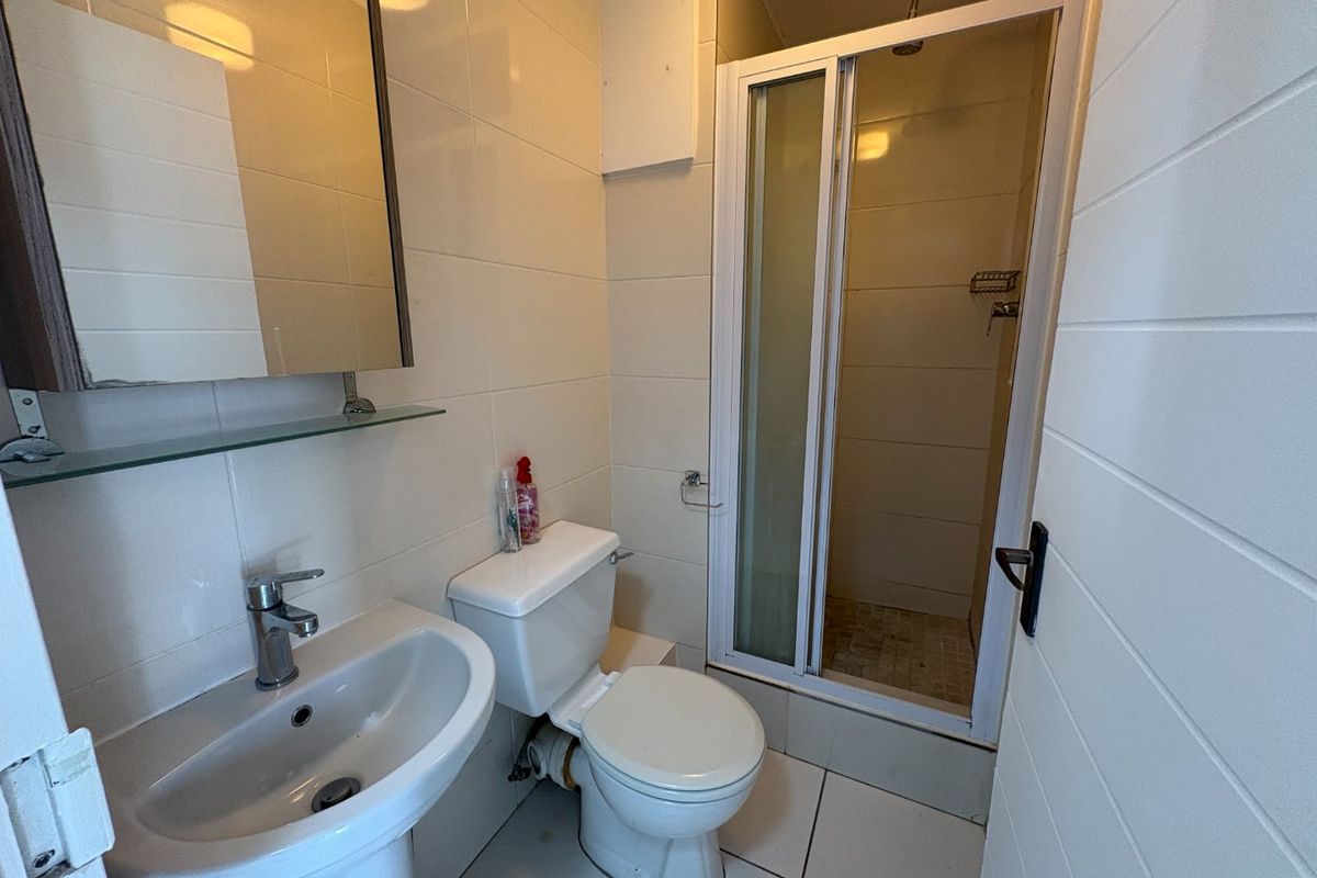 A functional bathroom featuring a pedestal basin, toilet, and a glass-enclosed shower with tiled finishes throughout.