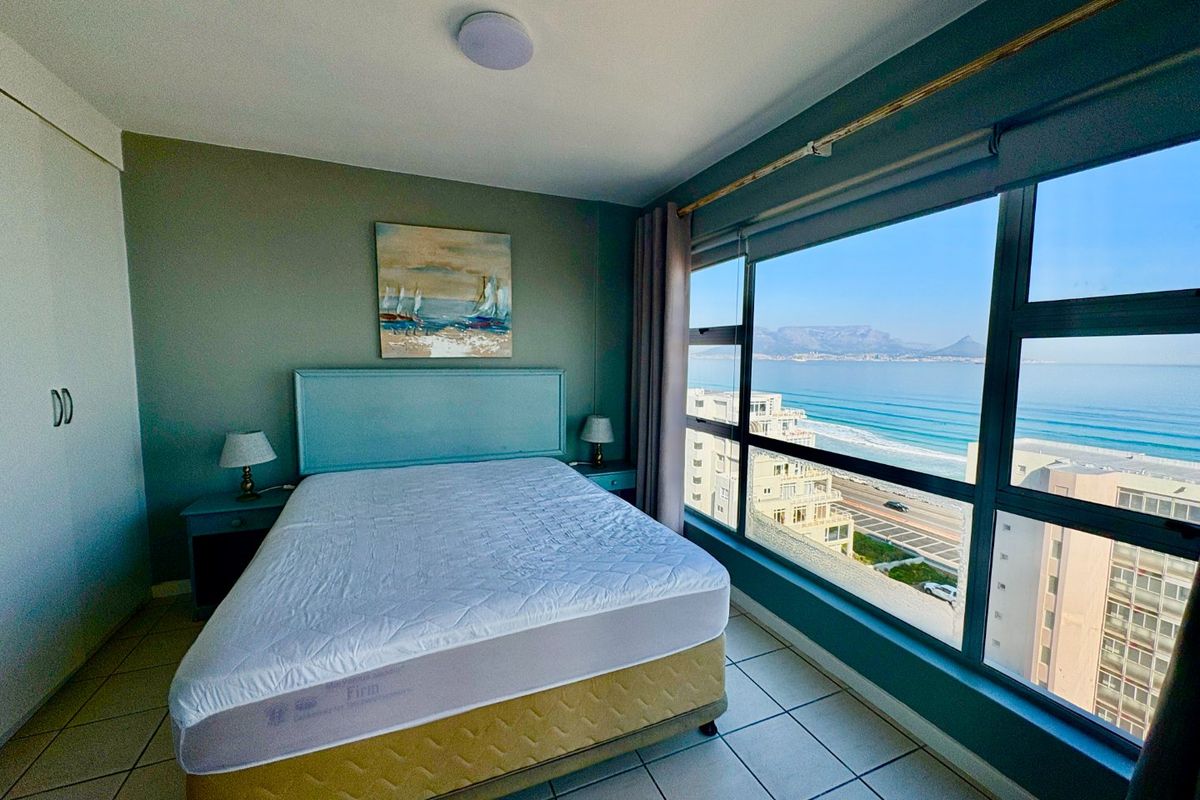 A bright bedroom featuring tiled floors, built-in storage, and a large window offering expansive ocean and mountain views.