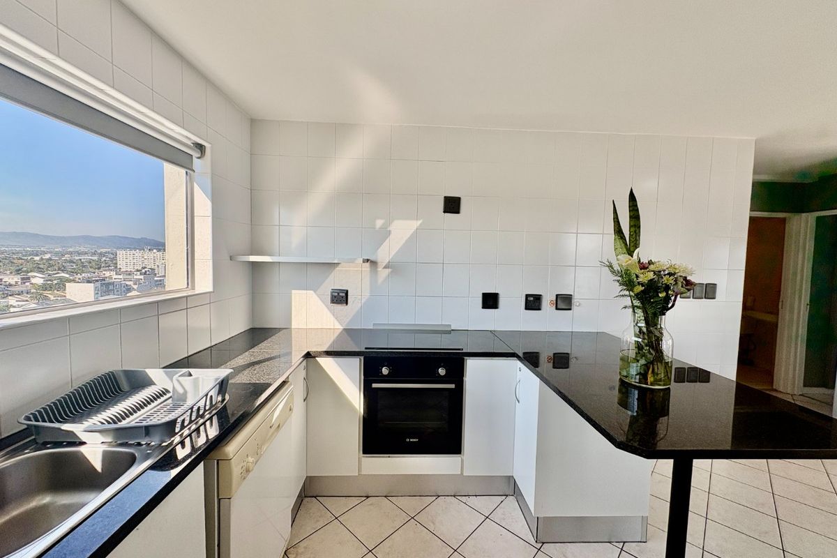 Modern kitchen featuring granite countertops, built-in oven, electric hob, and a breakfast bar with expansive city views.