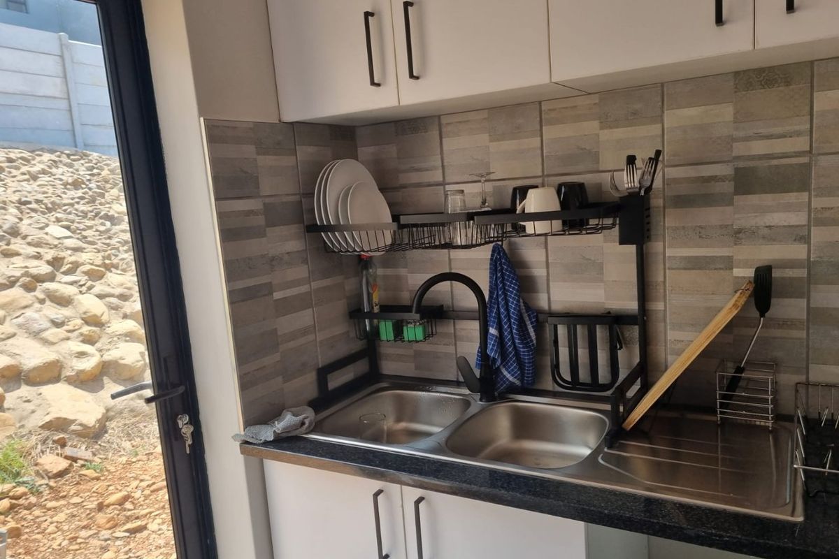 A compact kitchen area featuring a double bowl stainless steel sink, modern black mixer tap, tiled splashback, and white built-in cabinetry.