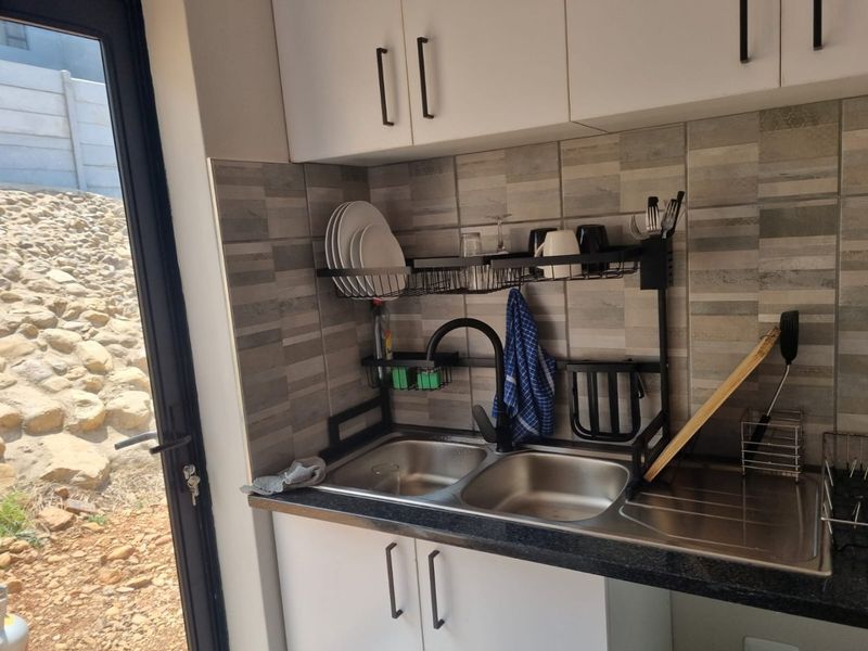 A compact kitchen area featuring a double bowl stainless steel sink, modern black mixer tap, tiled splashback, and white built-in cabinetry.