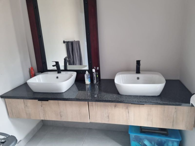 Modern bathroom vanity featuring a granite countertop, dual vessel sinks with black fixtures, and floating wood-finish cabinetry.