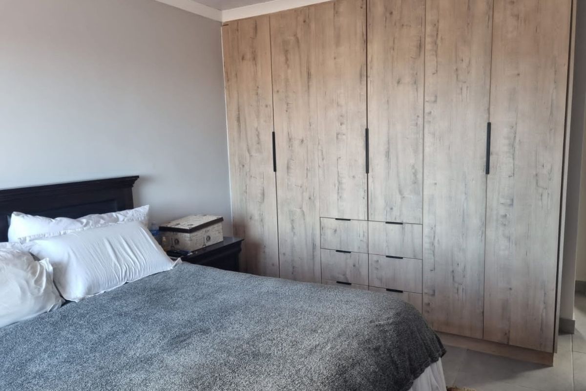 A well-maintained bedroom featuring modern wood-look built-in cupboards and neutral tiled flooring.
