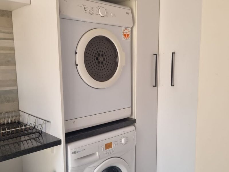 A compact laundry area featuring built-in cabinetry, a granite countertop, and a stacked washer and dryer configuration.