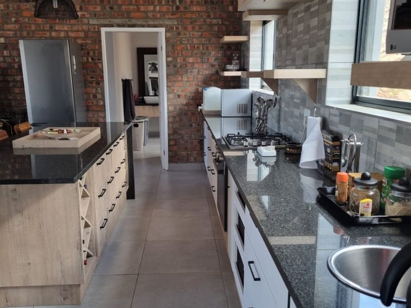 Modern kitchen featuring granite countertops, an island, exposed brick wall, and high-quality cabinetry with integrated appliances and tiled flooring.