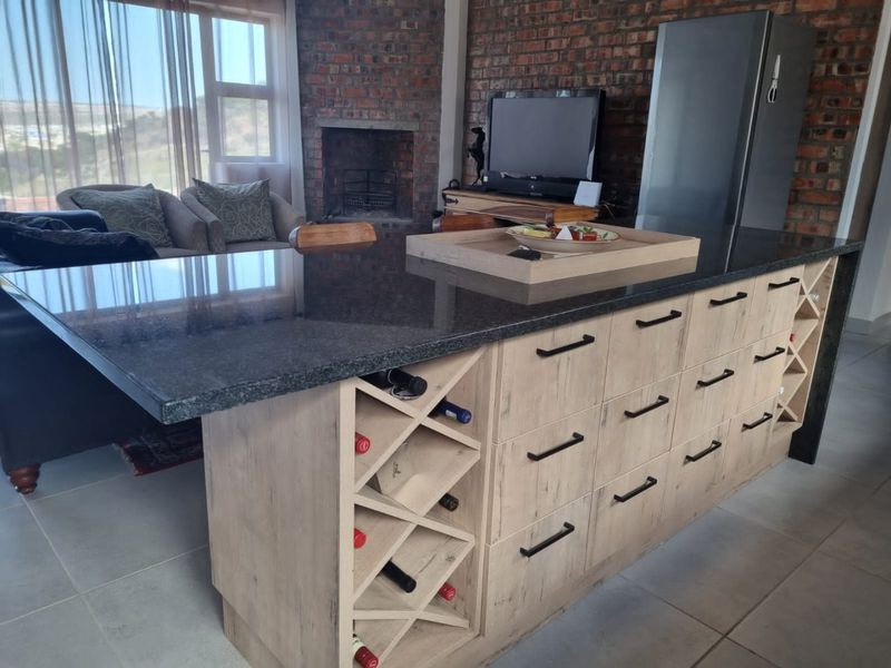Open plan living area featuring a large kitchen island with granite countertops, built-in wine storage, and an exposed brick wall with a fireplace.