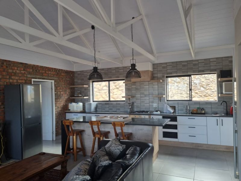 Spacious open-plan kitchen and living area featuring exposed white timber trusses, a striking brick feature wall, modern cabinetry, and a central kitchen island.