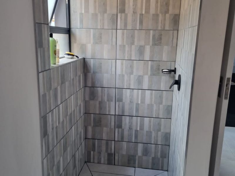 A modern walk-in shower featuring contemporary grey patterned wall tiles, a sleek black rain shower head, and a linear floor drain.