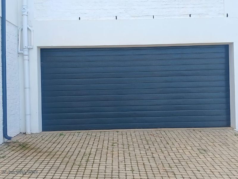 A view of a residential garage featuring a dark blue sectional door and a paved driveway area.