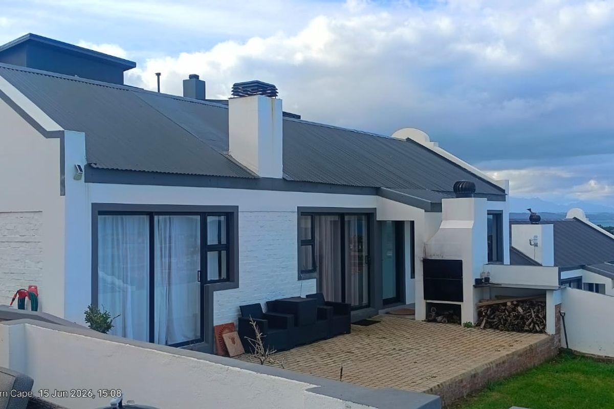 Rear exterior view of the house featuring a paved patio area with a built-in braai, sliding glass doors, and a corrugated metal roof.