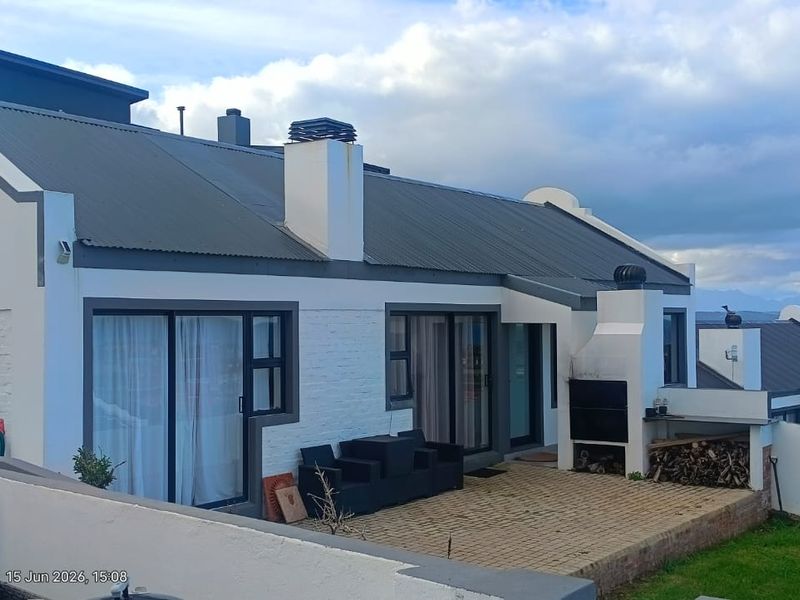 Rear exterior view of the house featuring a paved patio area with a built-in braai, sliding glass doors, and a corrugated metal roof.