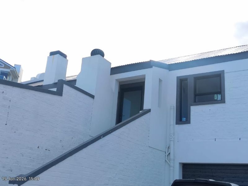 Front elevation of a modernised house featuring painted brickwork, corrugated metal roofing, and aluminium window frames.
