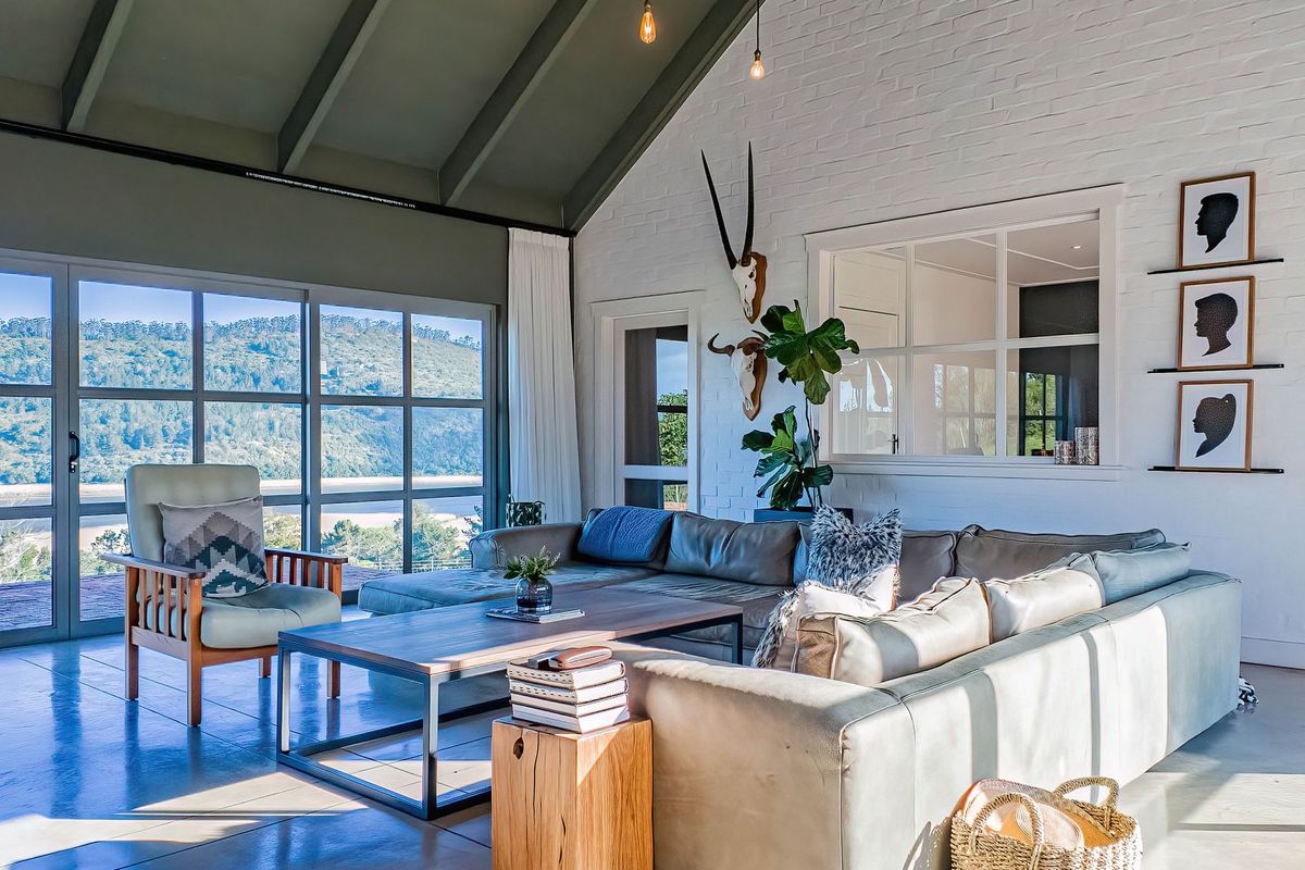 Spacious living room featuring a vaulted ceiling with exposed rafters, polished concrete floors, and large glass doors offering scenic landscape views.