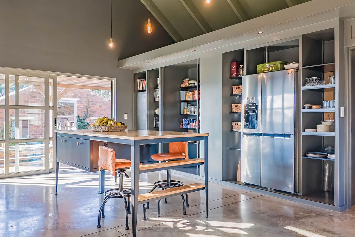 Modern farmhouse kitchen featuring a large central island, extensive built-in cabinetry with integrated shelving, and polished concrete floors under a high vaulted ceiling.