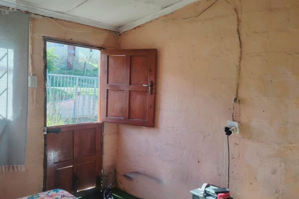 A bedroom featuring exposed masonry walls, a timber door leading outdoors, and visible electrical wiring requiring maintenance.