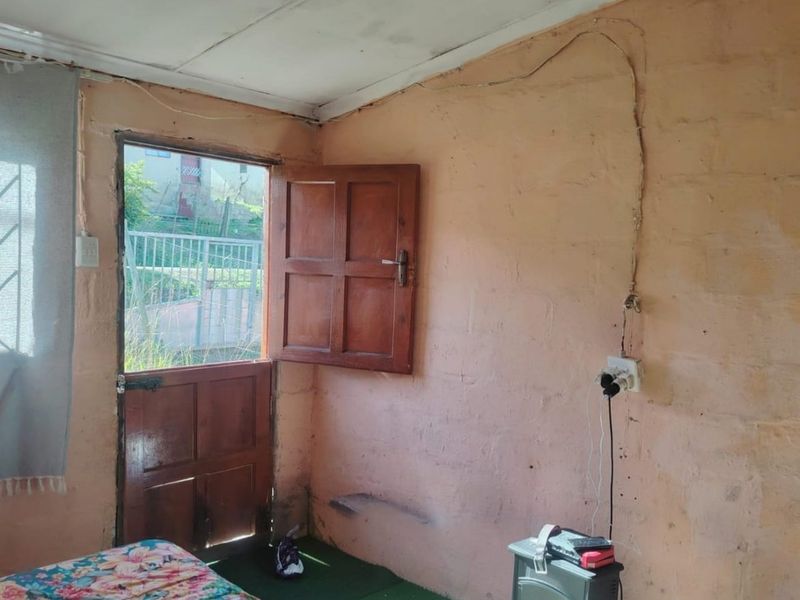 A bedroom featuring exposed masonry walls, a timber door leading outdoors, and visible electrical wiring requiring maintenance.