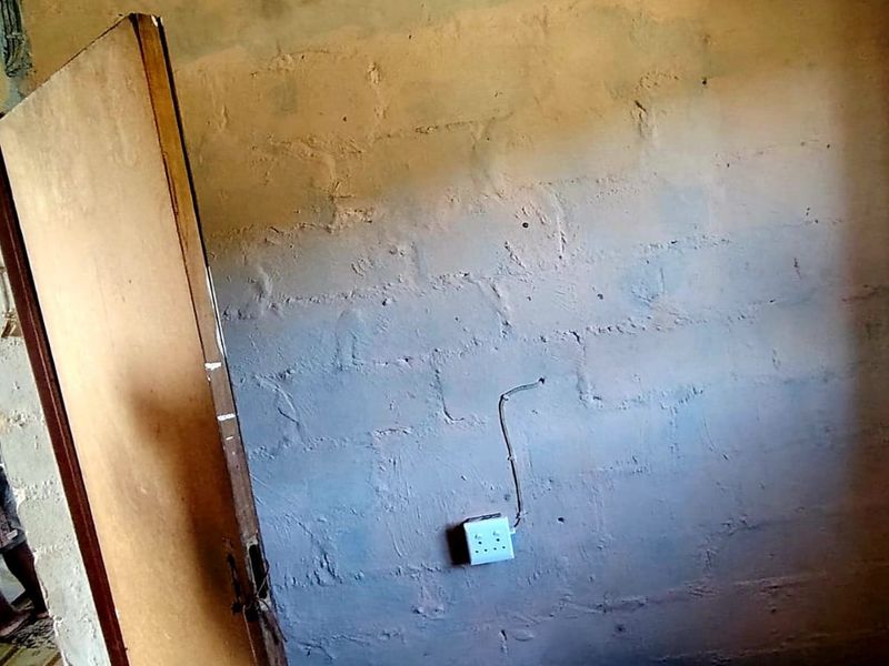 An unfinished interior room featuring exposed masonry walls, surface-mounted electrical wiring, and a basic door, requiring significant renovation and finishing work.