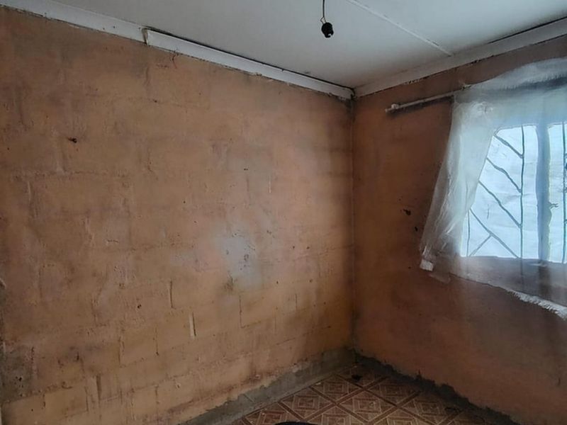 An empty bedroom featuring exposed brick walls, tiled flooring, and security bars on the window, requiring significant renovation and finishing work.