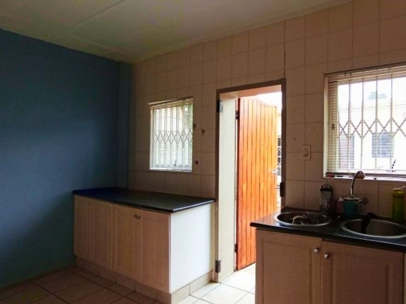 A functional kitchen space featuring built-in cabinetry, double sink, and tiled splashbacks, with direct access to the exterior.