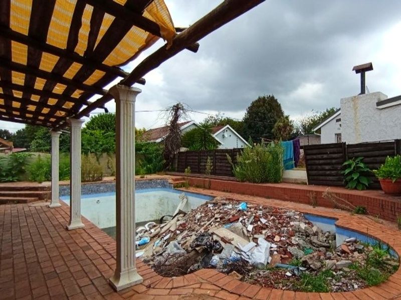 Outdoor pool area featuring a brick-paved patio and pergola, currently requiring significant clearing and restoration of the swimming pool structure.