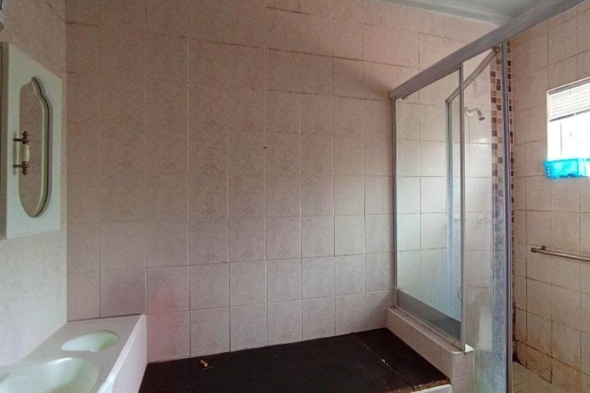 A dated bathroom featuring a shower enclosure, double vanity basin, and wall-mounted grab rail, requiring cosmetic updates to modernize the space.