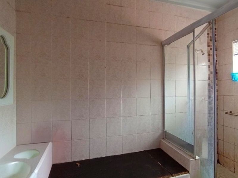 A dated bathroom featuring a shower enclosure, double vanity basin, and wall-mounted grab rail, requiring cosmetic updates to modernize the space.
