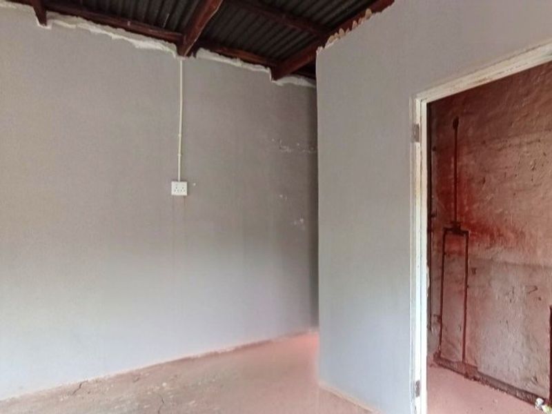 An unfinished utility space featuring exposed roof structure, raw wall finishes, and visible plumbing and electrical conduits, requiring significant renovation and finishing work.