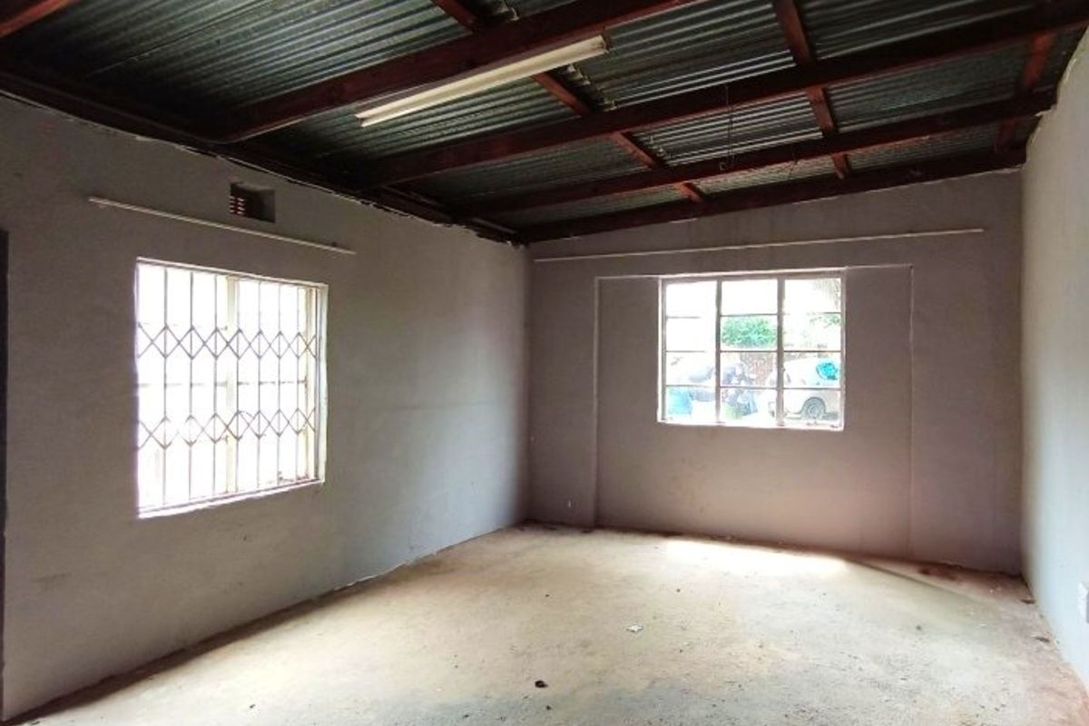 An empty, unfinished living area featuring exposed timber rafters, corrugated metal ceiling, and security burglar bars on the windows.