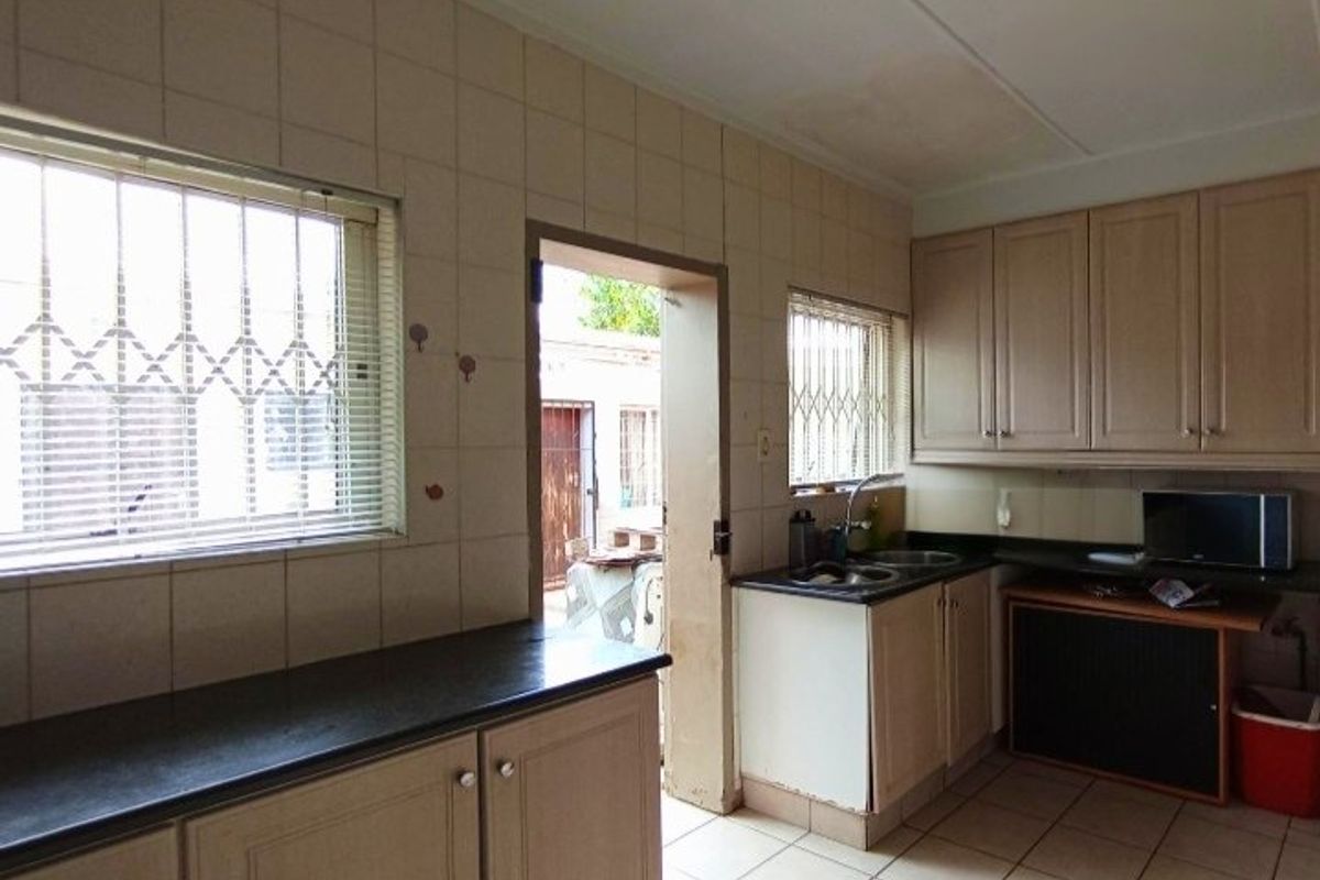 A functional kitchen featuring built-in cabinetry, laminate countertops, a double bowl sink, and tiled splashbacks with direct access to the exterior.