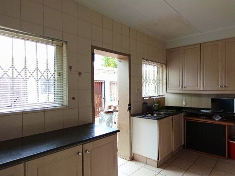 A functional kitchen featuring built-in cabinetry, laminate countertops, a double bowl sink, and tiled splashbacks with direct access to the exterior.