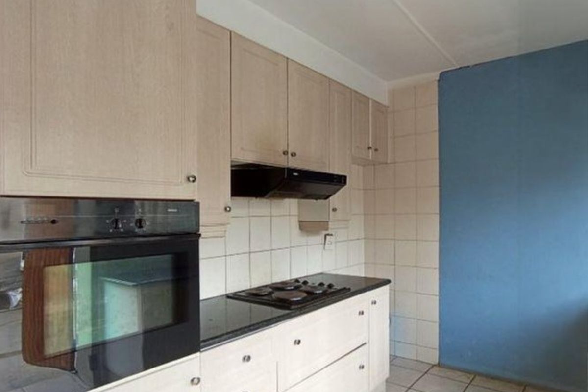 A functional kitchen featuring built-in cabinetry, an integrated oven, hob, and extractor fan, complemented by tiled flooring and a tiled backsplash.