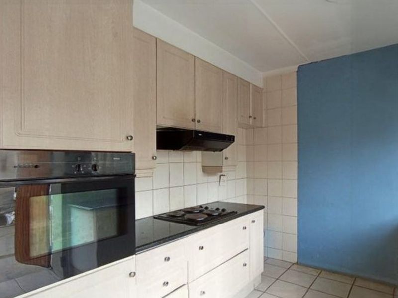 A functional kitchen featuring built-in cabinetry, an integrated oven, hob, and extractor fan, complemented by tiled flooring and a tiled backsplash.