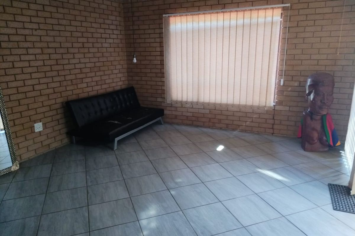 A living area featuring exposed brick walls, tiled flooring, and vertical blinds, offering a blank canvas for potential interior design updates.