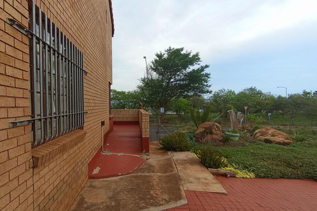 Exterior view of the property featuring a face brick facade, security bars on windows, and a paved walkway leading through the garden area.