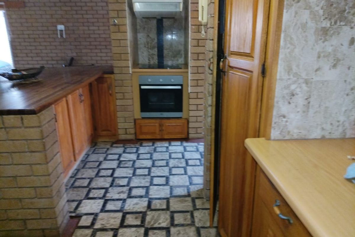 A rustic kitchen featuring brick-built cabinetry, wooden cupboards, a built-in oven with extractor fan, and distinctive stone tile flooring.