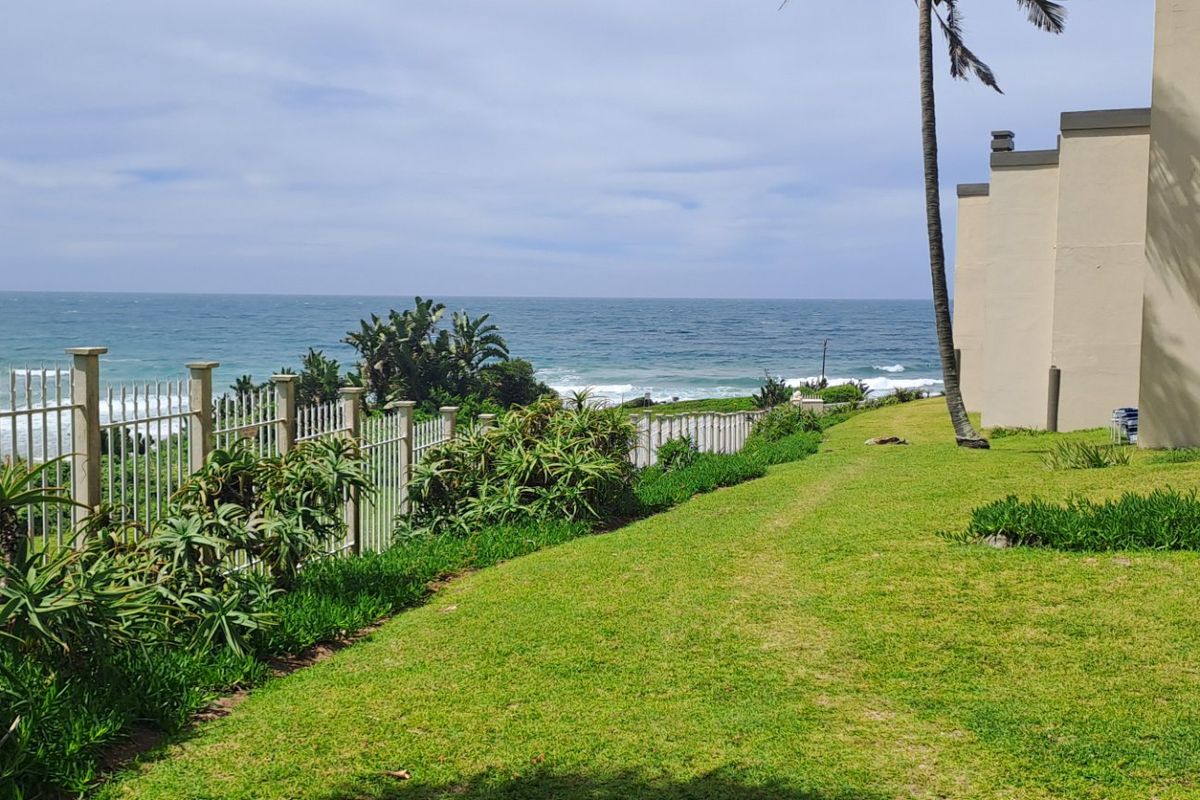A well-maintained rear garden area featuring a lawn, perimeter fencing, and direct views of the ocean.